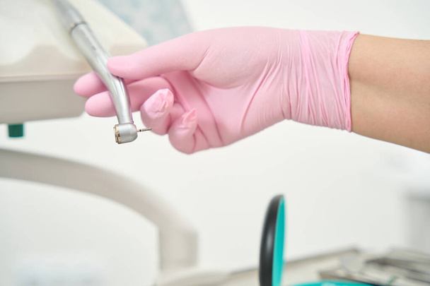 Ruka bělošského lékaře v růžové rukavici drží vrtačku - Fotografie, Obrázek