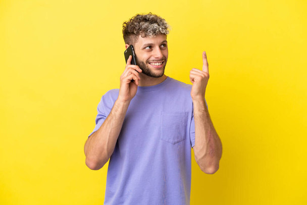 Young caucasian man using mobile phone isolated on yellow background pointing up a great idea - Foto, Imagem