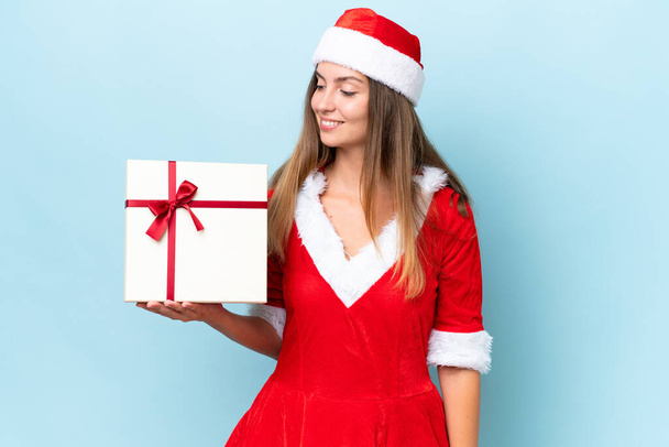 Anne Noel gibi giyinmiş beyaz bir kadın elinde hediyesiyle mavi arka planda mutlu bir ifadeyle izole edilmiş. - Fotoğraf, Görsel
