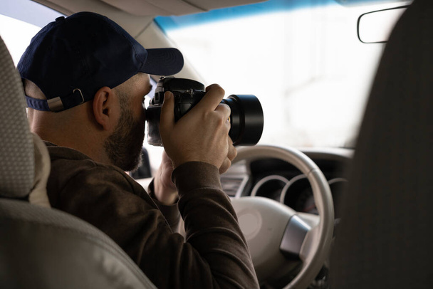 Magánnyomozó ül az autóban csinál megfigyelési munka fényképezés kamerával, belső nézet - Fotó, kép