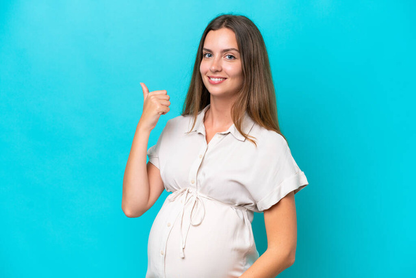 Mladá běloška žena izolované na modrém pozadí těhotná a s palcem nahoru - Fotografie, Obrázek