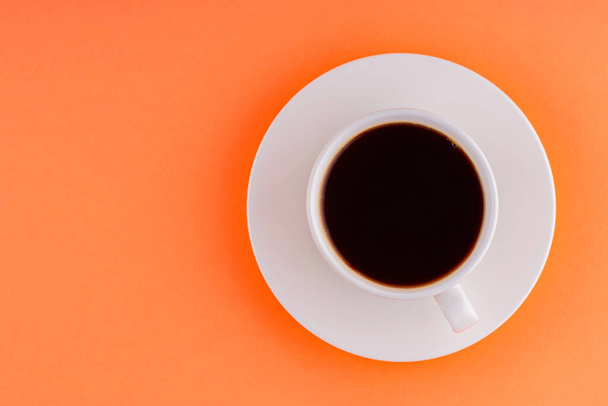 Cup of coffee on orange background. White cup of black coffee on a white saucer. Copy space. Top view - Fotoğraf, Görsel