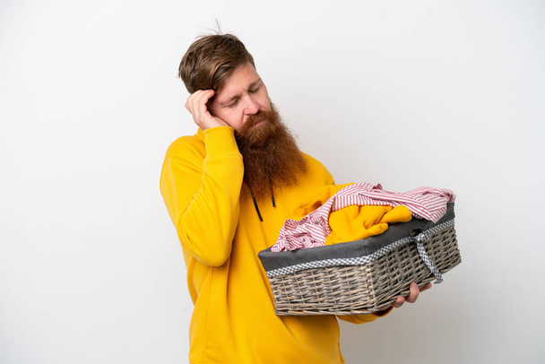 Redhead man with beard holding a clothes basket isolated on white background with headache - Foto, immagini