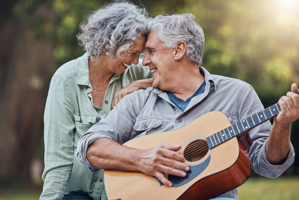 Starsza para, gitara i miłość w parku razem grając romantyczną, miłosną lub uczuciową piosenkę muzyczną dla żony. Romans, emerytowany starszy mężczyzna i kobieta grają na instrumencie smyczkowym i śmieją się w lesie na świeżym powietrzu. - Zdjęcie, obraz