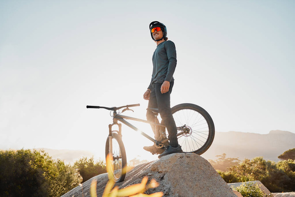 Ποδήλατο βουνού ή μοτοσυκλέτα ποδηλάτης σε βράχο για μαραθώνιο στόχο, αθλητικές περιπέτειες ή υπαίθρια ταξίδια με γυαλιά ηλίου και κράνος. Fitness άνθρωπος κατάρτισης με ποδήλατο σε ένα λόφο μπλε ουρανό mockup στην Αυστραλία. - Φωτογραφία, εικόνα