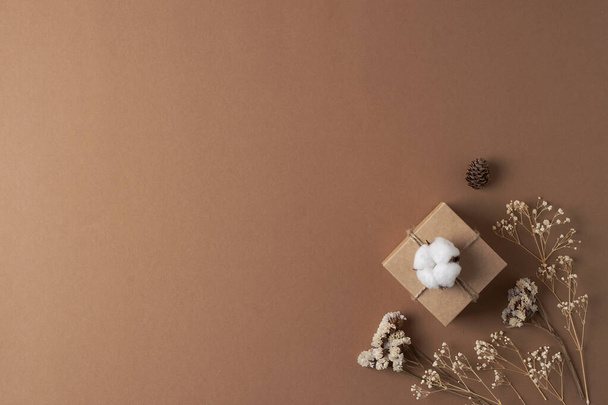 Decoraciones navideñas con regalo y flores sobre fondo marrón. Colocación plana, espacio de copia - Foto, Imagen