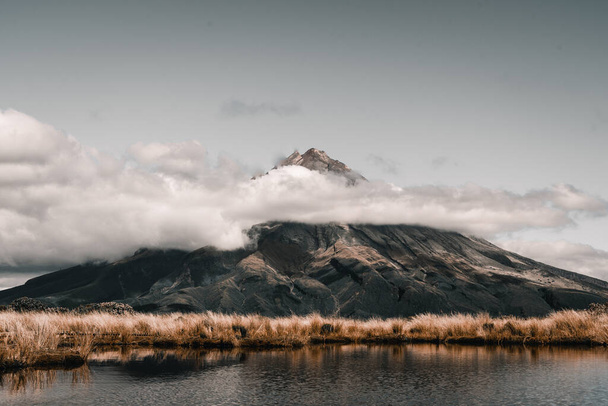 miękka roślinność otaczająca jezioro i imponująca góra w pięknym krajobrazie przyrody wraz z niebem z wieloma chmurami, taranaki, Nowa Zelandia - koncepcja podróży - Zdjęcie, obraz