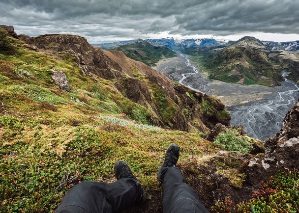夏にアイスランドのソルスモークで暗い嵐の空と山の上でリラックスした旅行者の足 - 写真・画像
