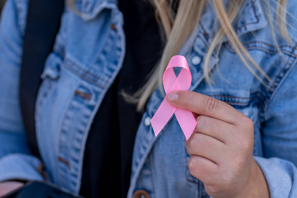 woman in a denim jacket holding a pink satin ribbon in her hand. - Photo, Image