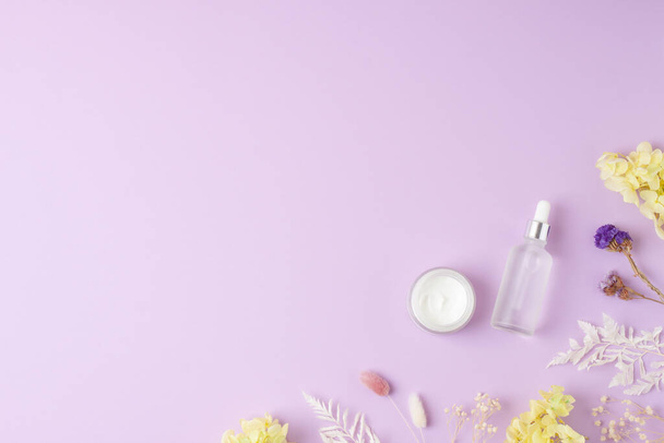Productos cosméticos para el cuidado de la piel con flores sobre fondo rosa. Colocación plana, espacio de copia - Foto, imagen