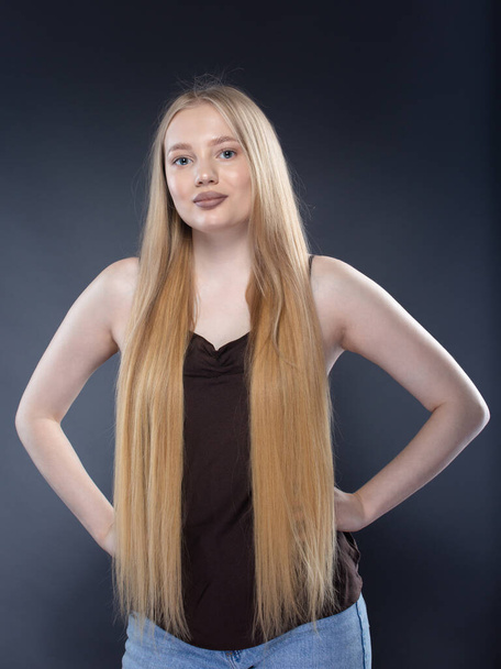Young blonde woman in jeans and brown singlet on dark gray background - Fotografie, Obrázek