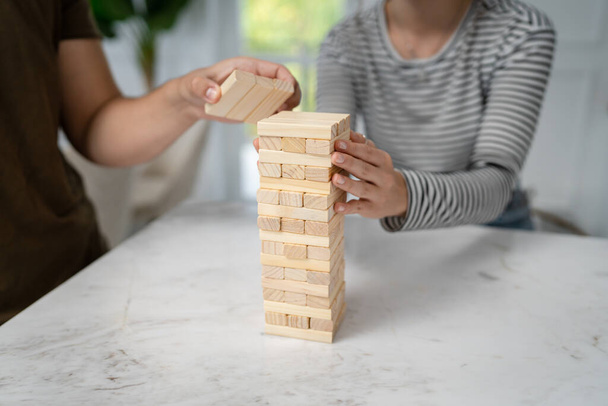close up hand of unknown Caucasian woman stacking bricks for jenga game wooden pieces making tower close up copy space family leisure board game - Foto, afbeelding
