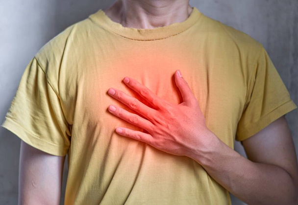 Asian young man suffering from central chest pain. Chest pain can be caused by heart attack, myocardial infarct or ischemia, myocarditis, pneumonia, oesophagitis, stress, etc,. - Photo, Image