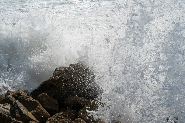 Une vague de mer se brise sur quelques rochers, créant de la mousse et des gouttes d'eau. - Photo, image