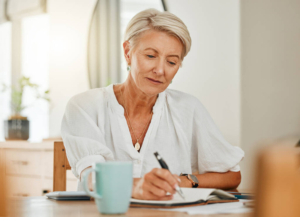 Γράφοντας, σκεπτόμενη και ηλικιωμένη γυναίκα σε ένα σπίτι που κρατάει σημειώσεις σε σημειωματάριο. Συνταξιοδότηση ενός σοβαρού προσώπου από τη Σουηδία σκεφτείτε το χρονοδιάγραμμα, την ημερήσια διάταξη ιδέα ή έγγραφο και γράψτε ιδέες στο σπίτι. - Φωτογραφία, εικόνα