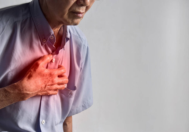 胸の痛みに苦しむアジア系の老人。胸痛は、心臓発作、心筋梗塞や虚血、心筋炎、肺炎、食道炎、ストレス、不安などによって引き起こされる可能性があります。,. - 写真・画像