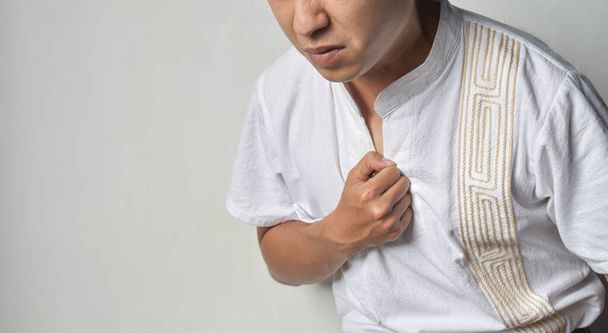 Asian young man suffering from central chest pain. Chest pain can be caused by heart attack, myocardial infarct or ischemia, myocarditis, pneumonia, oesophagitis, stress, anxiety, etc,. - Photo, Image
