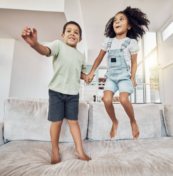 Children, brother and sister bonding and jumping on sofa in house, home or hotel living room in fun, play and energy game. Smile, happy or adhd kids or hyperactive Mexico boy and girl with sugar rush. - Photo, Image