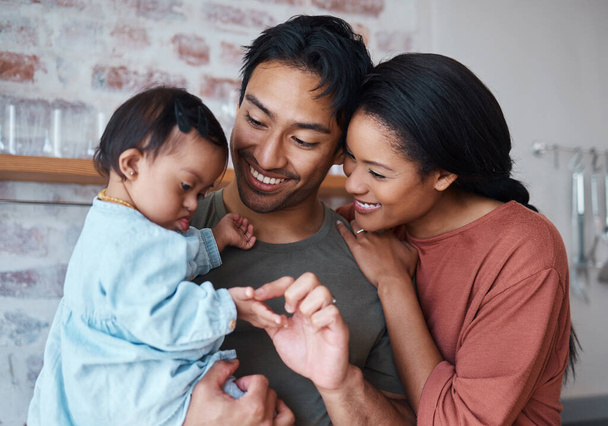 Familie mit Down-Syndrom-Baby, glückliche Eltern im gemeinsamen Haushalt und Kleinkindbetreuung. Indischer Vater hält süßes Kind, asiatische Mutter lächelt mit Unterstützung und bindendem Glück in Brasilien Haus. - Foto, Bild