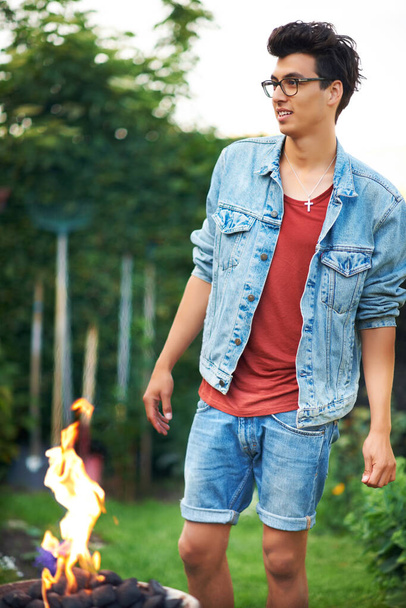 Going on a camping trip. Handsome young guy standing outside near a campfire - Fotografie, Obrázek