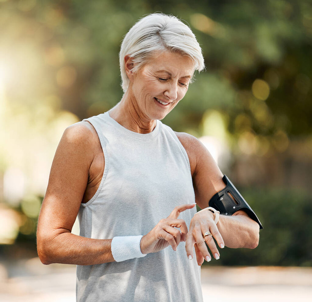 Senior woman, fitness and watch of running time in health and wellness for cardio exercise in nature. Active elderly female runner checking smartwatch to monitor training results in sports workout. - Foto, immagini