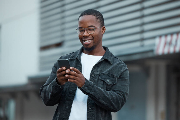 Hombre negro, teléfono y redes sociales en la ciudad leyendo mensajes de texto o comunicación en la aplicación de redes sociales. Persona afroamericana, conversación de chat y feliz en el teléfono inteligente móvil 5g en Atlanta sonrisa. - Foto, Imagen