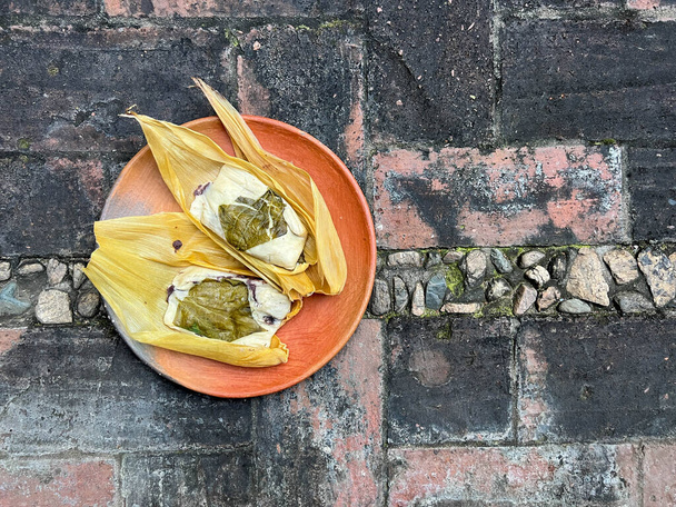 Two Oaxacan tamales with hoja santa wrapped on the outside of the masa and filled with beans with brick background - Photo, Image