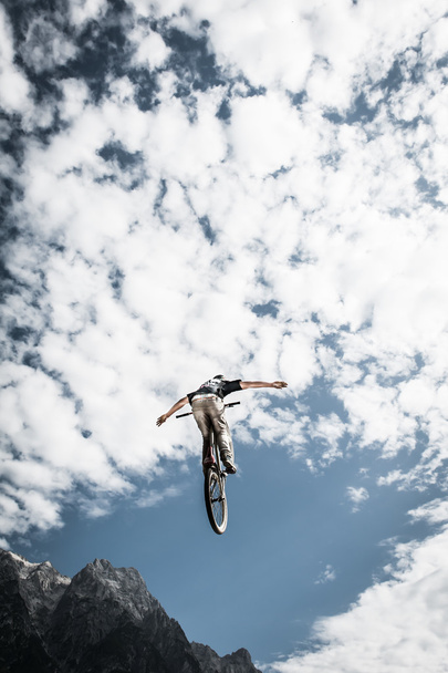 Каскадний брудний велосипедист з руками вільний високо в хмарному небі і горах
 - Фото, зображення