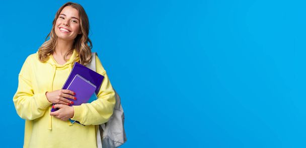 Carismática mujer europea alegre llevar mochila y cuadernos como ir próxima conferencia, sonriendo feliz, disfrutando de estilo de vida estudiantil, estudiar en la universidad, de pie fondo azul
. - Foto, imagen
