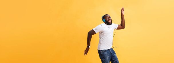 Pełna długość Portret wiśnia młodego człowieka african american słuchanie muzyki przez słuchawki i taniec na białym tle nad żółtym tle. - Zdjęcie, obraz
