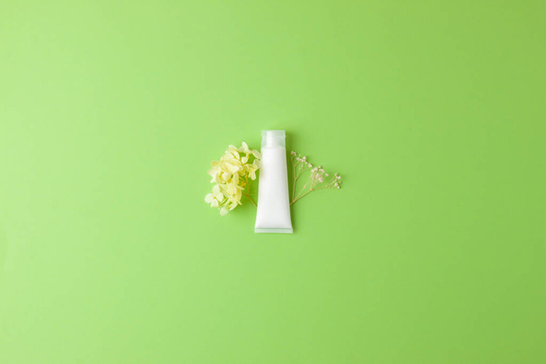 White tube of cosmetic cream with flowers on green background. Flat lay, copy space - Zdjęcie, obraz