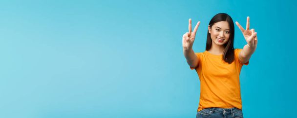 Positive upbeat cute asian girl believe win, aim success extend hands show victory, peace sign smiling broadly, have happy enthusiastic mood, spend carefree vacation travel abroad value pacifism. - Photo, Image