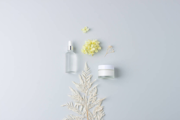 Productos cosméticos para el cuidado de la piel con flores sobre fondo gris. Colocación plana, espacio de copia - Foto, imagen