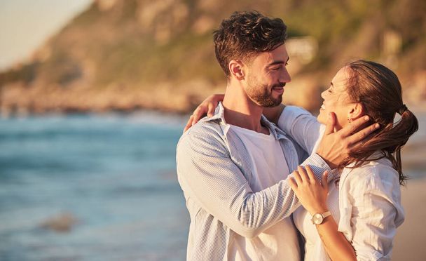 Love, beach and couple embrace at sunset for romantic summer evening date together in nature. Happy, sweet and satisfied people in relationship make eye contact for affection and care - Zdjęcie, obraz
