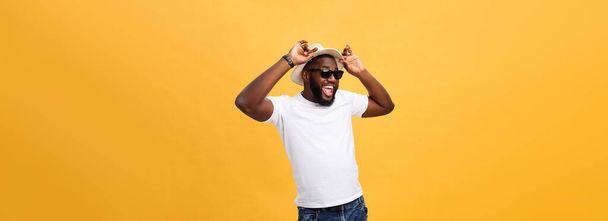 Close up portrait of a young man laughing with hands holding hat isolate over yellow background. - Foto, Imagen
