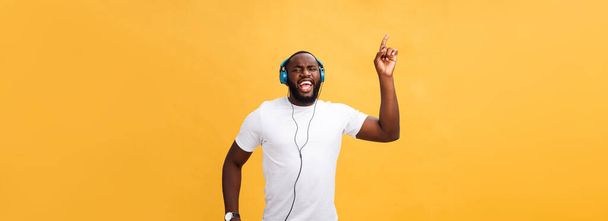 Jonge African American man dragen hoofdtelefoon en geniet van muziek dansen over geelgoud achtergrond. - Foto, afbeelding