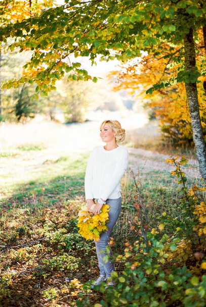 Šťastná žena s kyticí žlutých listů stojí u stromu. Kvalitní fotografie - Fotografie, Obrázek