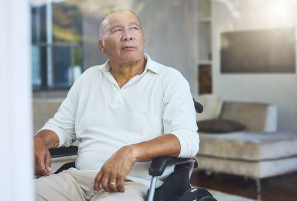 Disabled, sad and senior man thinking of accident in a wheelchair by the window in the living room in his house. Elderly man with depression, disability and retirement idea in a nursing home. - Foto, Bild