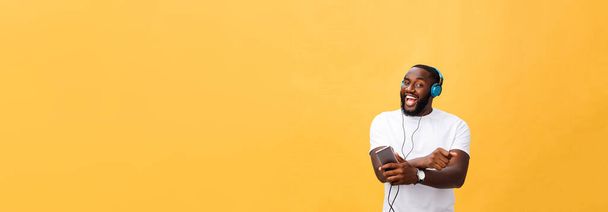 Un Afro-Américain avec écouteurs écoute et danse avec de la musique. Isolé sur fond jaune
. - Photo, image