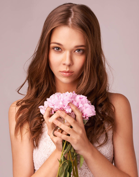 Innocence and beauty. Beautiful young woman holding a bunch of pink flowers against a pink background - Фото, изображение