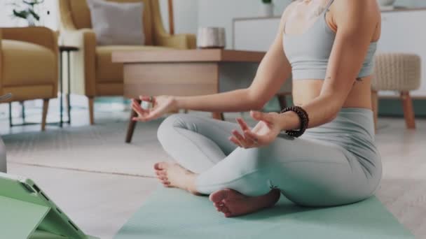 Jooga, zen ja meditaatio naisen kanssa urheilija istuu jalat ristissä matolla olohuoneessa kotinsa. Hyvinvointi, terveys ja meditointi nuoren naisen kanssa talossaan kuntoiluun tai liikuntaan. - Materiaali, video