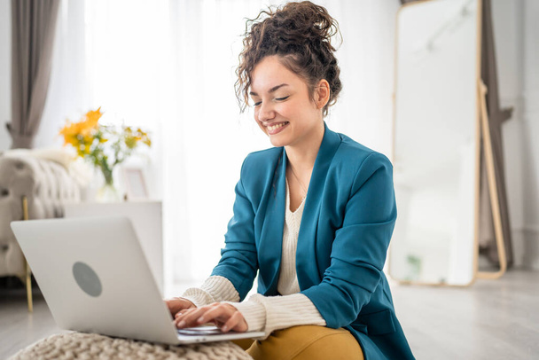 Yksi nainen nuori aikuinen valkoihoinen nainen istuu lattialla kotona kannettavan tietokoneen kanssa ja etsii sivulle onnellinen hymy freelance brunette kiharat hiukset kotielämä kopioi tilaa - Valokuva, kuva