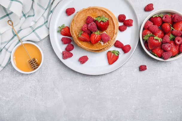 Tasty pancakes served with honey and berries on light grey table, flat lay. Space for text - Foto, afbeelding