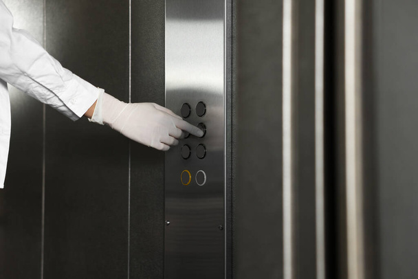 Woman wearing medical glove choosing floor in elevator, closeup. Protective measure - Valokuva, kuva