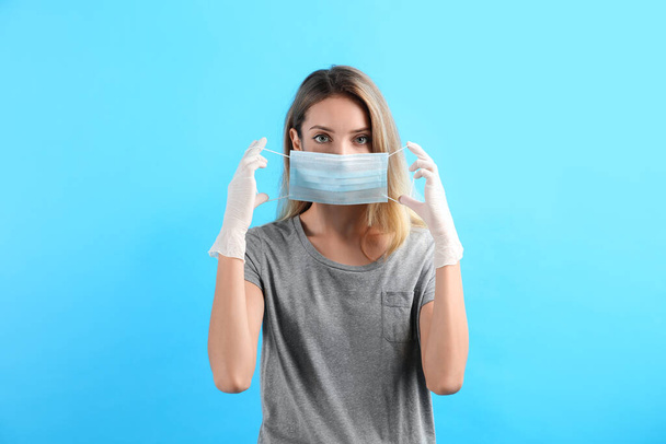 Woman in medical gloves putting on protective face mask against light blue background - Photo, Image