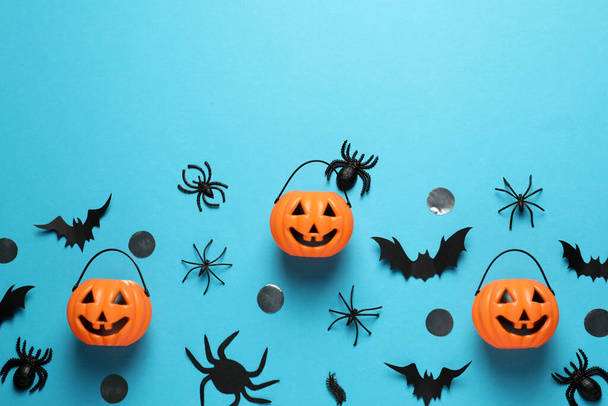 Flat lay composition with plastic pumpkin baskets, paper bats and spiders on light blue background, space for text. Halloween celebration - Photo, Image