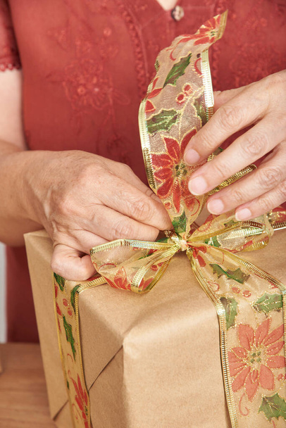 Close up view of female hands making a bow with a decorative ribbon for decorating a Christmas gift. Concept of wrapping holidays presents. - Fotoğraf, Görsel