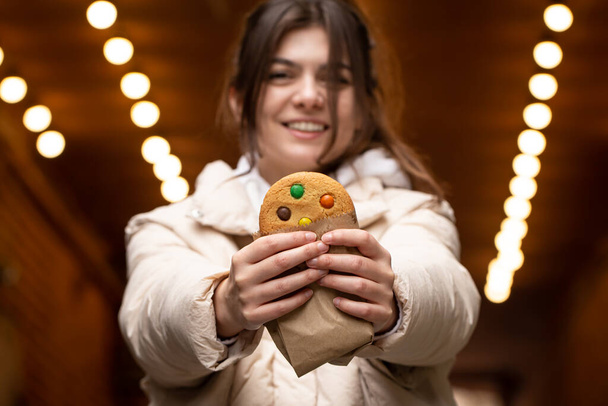 Attraktive junge Frau mit einem Lebkuchen in der Hand, einem schönen bunten Lebkuchen in der Hand einer Frau, einem Stadtspaziergang. - Foto, Bild