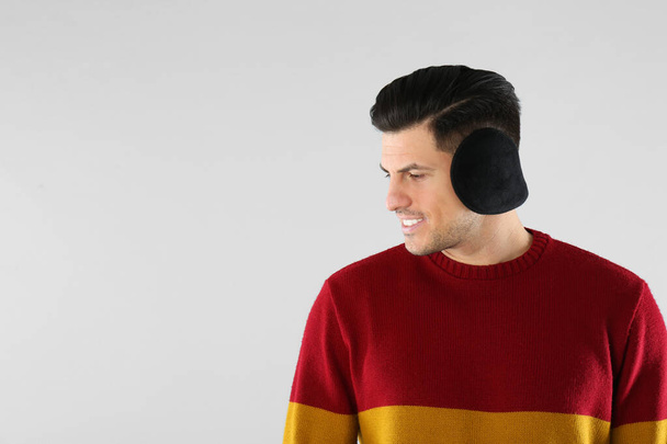 Man wearing stylish earmuffs on light background. Space for text - Foto, immagini
