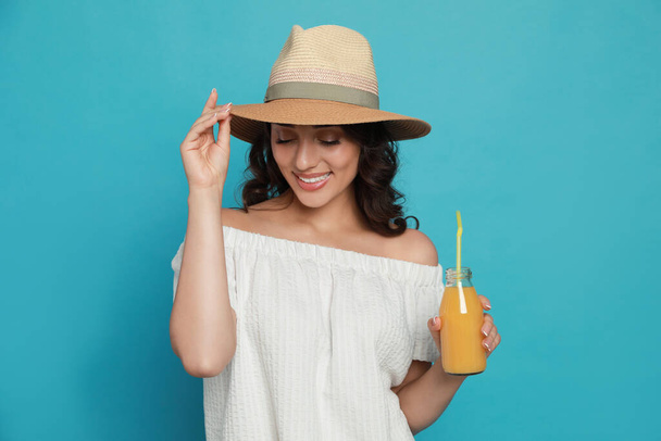 Beautiful young woman with straw hat and bottle of refreshing drink on light blue background - Foto, Imagem